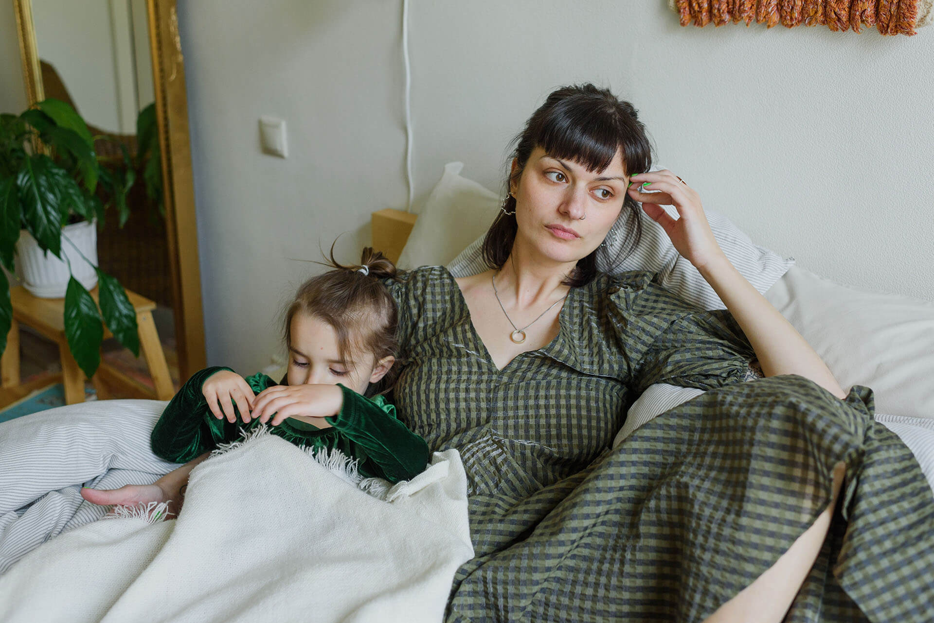 Young mom feeling stressed and exhausted sitting with her young daughter on the bed.