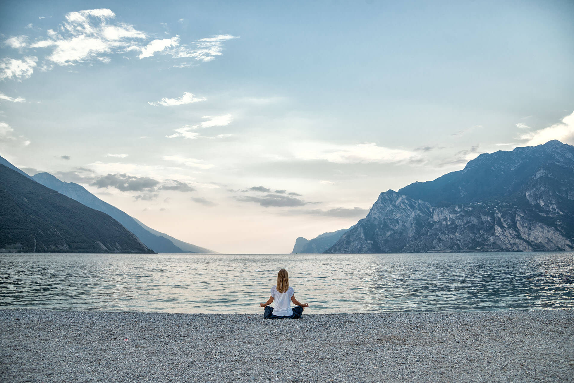 Young woman sitting on a stony beach at a mountain lake breathing in and practicing mindfulness