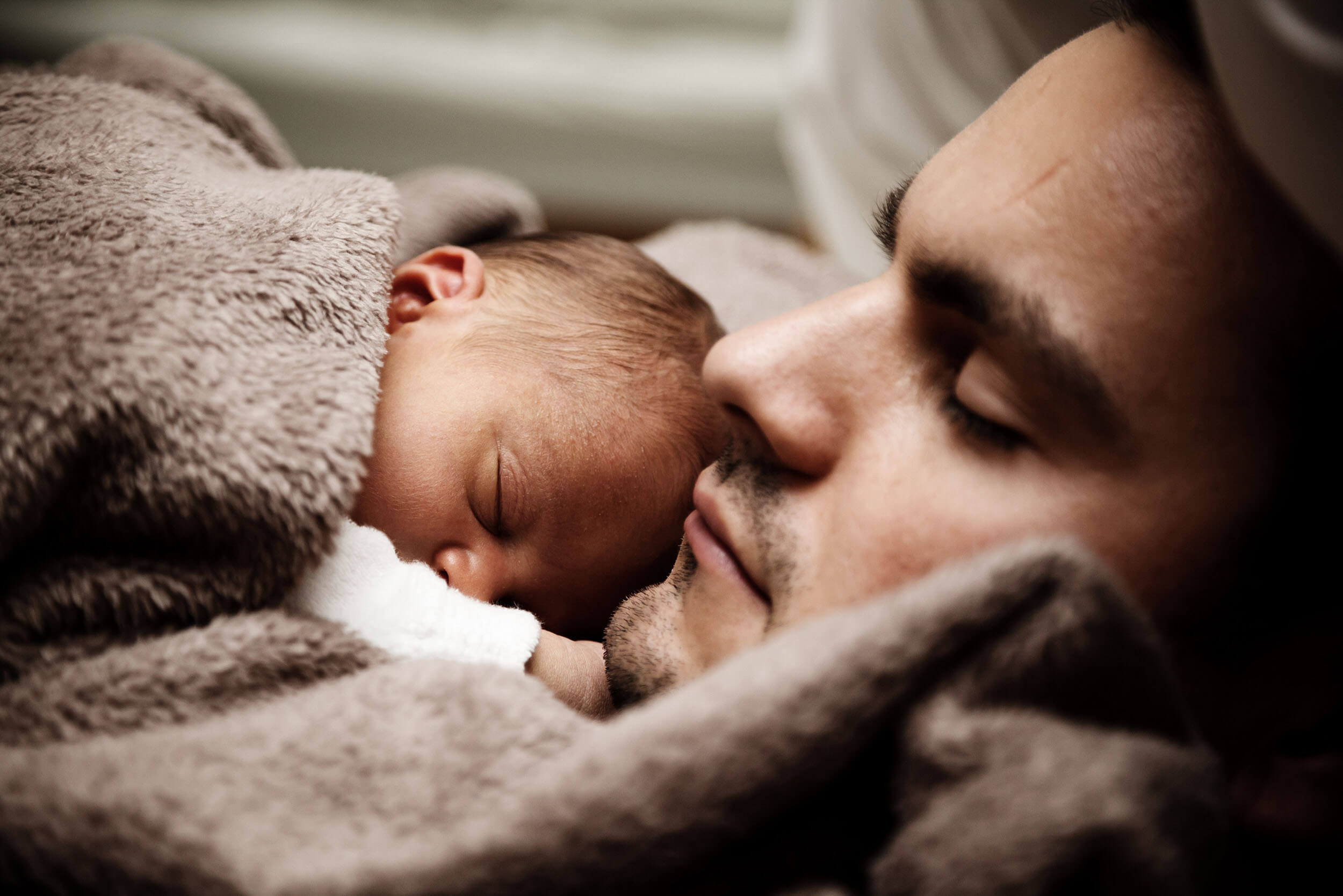 Father learning how to breathe while lying down cuddling his sleeping newborn baby