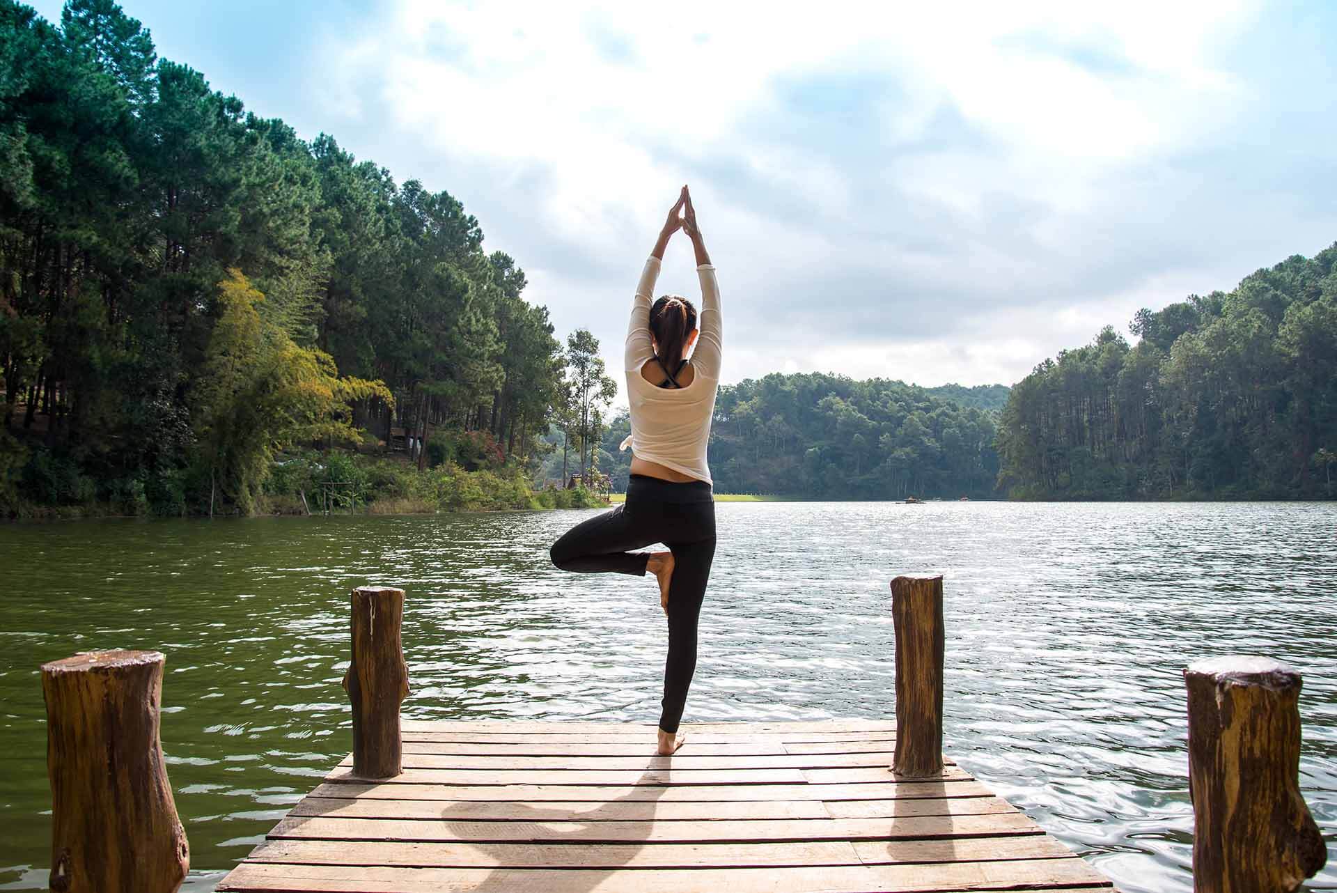 Woman balancing in a yoga pose on a mountain lake pier.