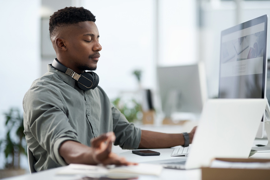 Young business man meditating and doing breathwork at his desk.