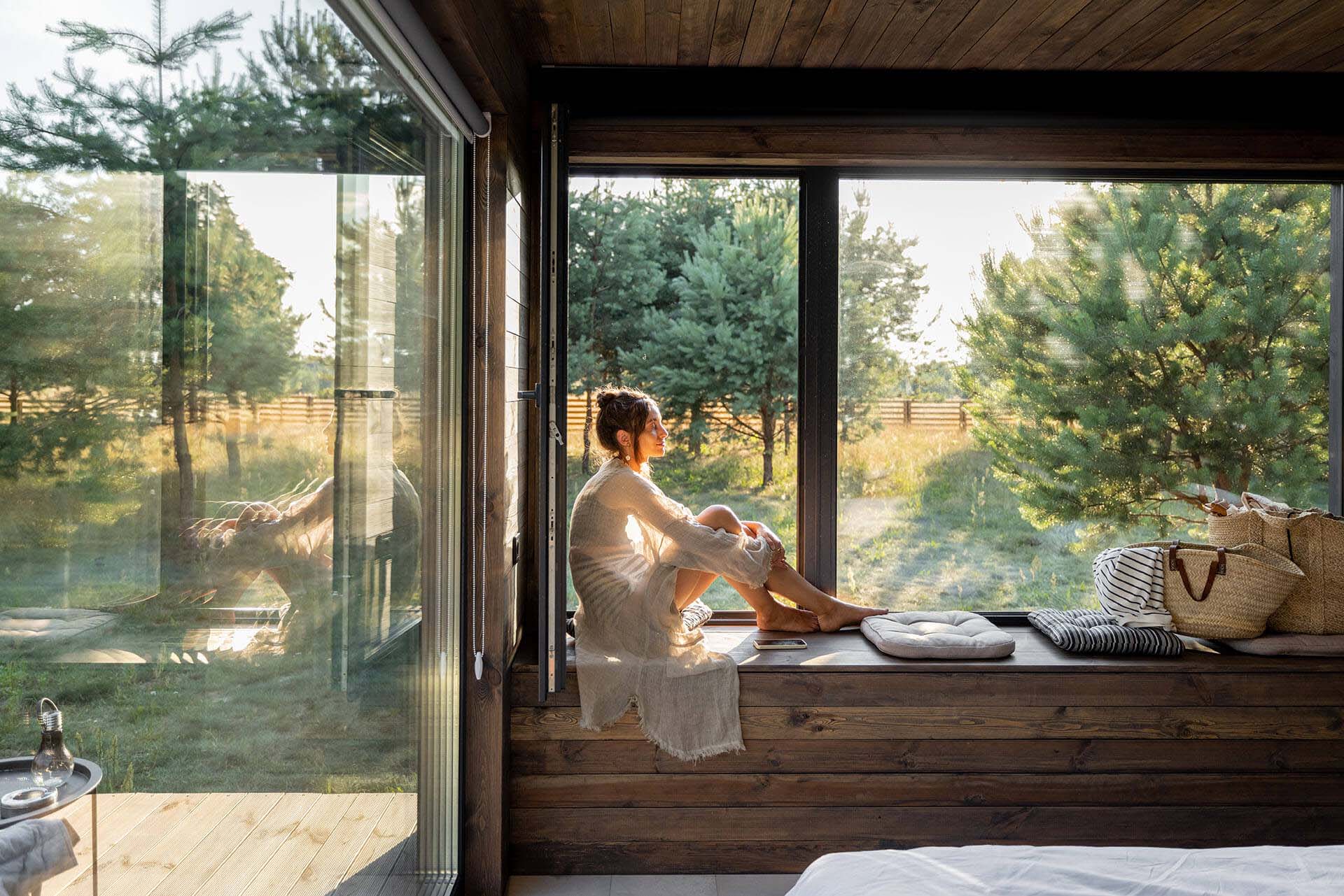 Woman sitting at her bedroom window in the forest learning how to relax in her every day life.