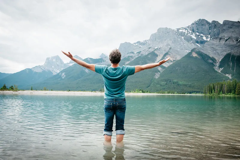 Man standing in a mountain lake with arms stretched out practicing mindfulness and breathwork.